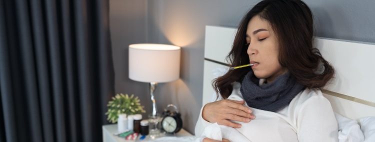 kranke Frau mit Kopfschmerzen liegt mit Fieberthermometer im Bett