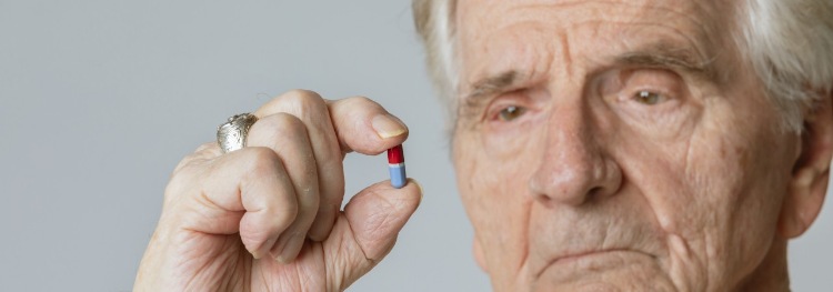 Älterer Mann hält eine Arzneimittelkapsel zwischen seinen Fingern