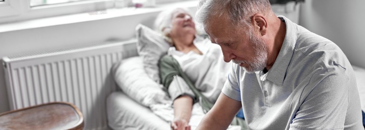 Trauriger alter Mann sitzt am Bett seiner kranken Ehefrau