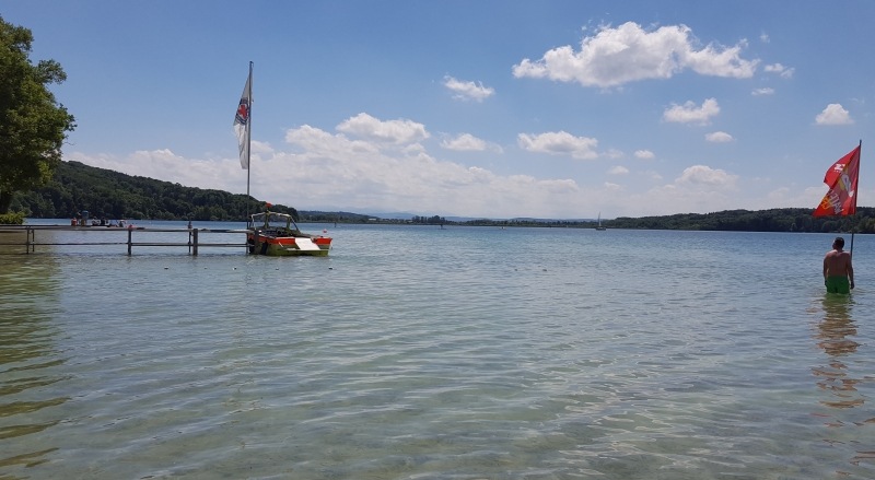Badesee mit Steg Motorboot und Flagge der Wasserwacht