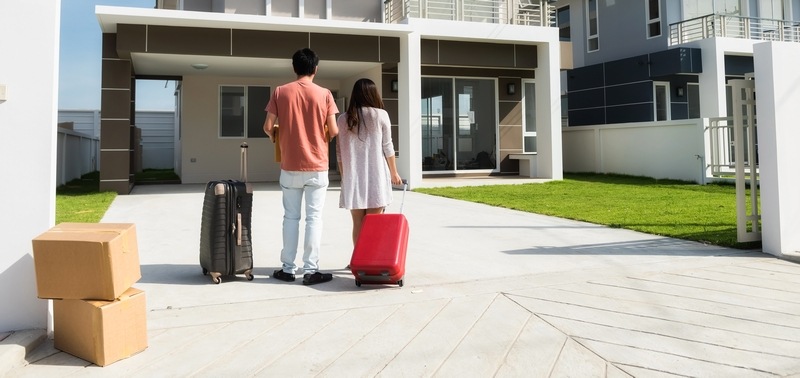 Paar steht mit Koffern und Umzugskartons vor einem Haus