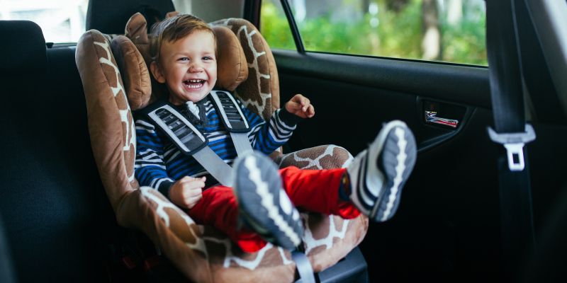 Kleiner Junge sitzt im Auto im Kindersitz und lacht