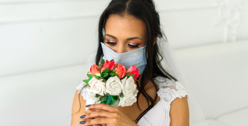 Traurige Braut mit Cornona Schutzmaske hält einen Brautstrauß