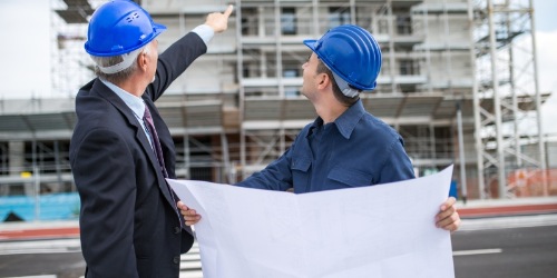 Bauingenieur und Architekt mit Plan vor einer Baustelle