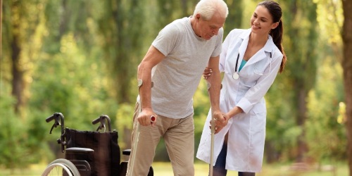 Ärztin hilft älterem Mann auf Gehhilfen zu stehen