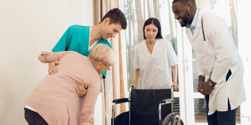 Pfleger helfen einer alten Dame in den Rollstuhl