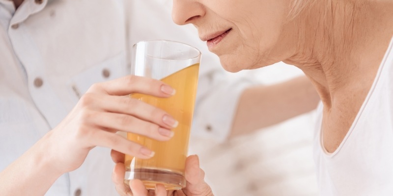 Krankenpflegerin reicht älterer Dame ein Glas Saft