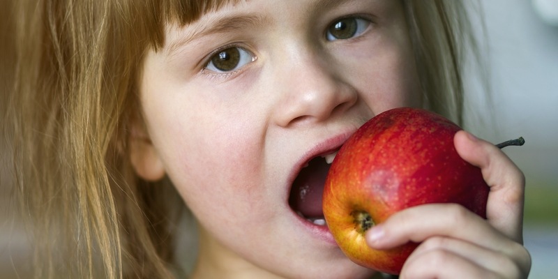 kleines Mädchen beisst in einen Apfel
