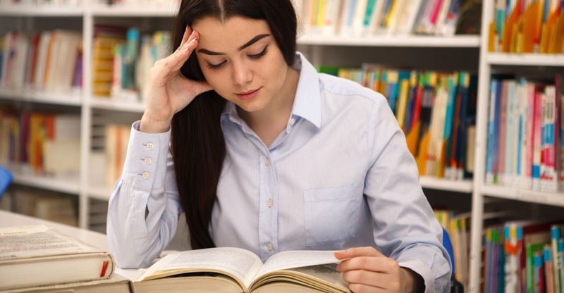 Frau studiert in einer Bibliothek in einem dicken Buch