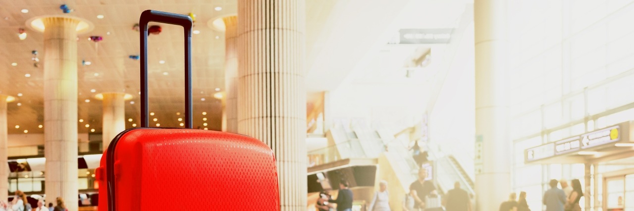 roter Rollkoffer im Wartebereich eines Flughafenterminals