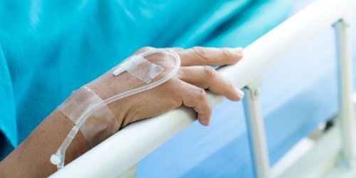 Hand eines Patienten im Krankenhausbett mit Infusion