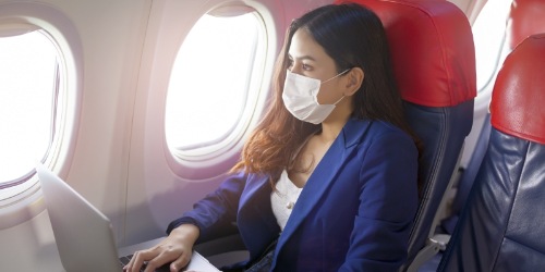Geschäftsreisende mit Laptop und Maske im Flugzeug