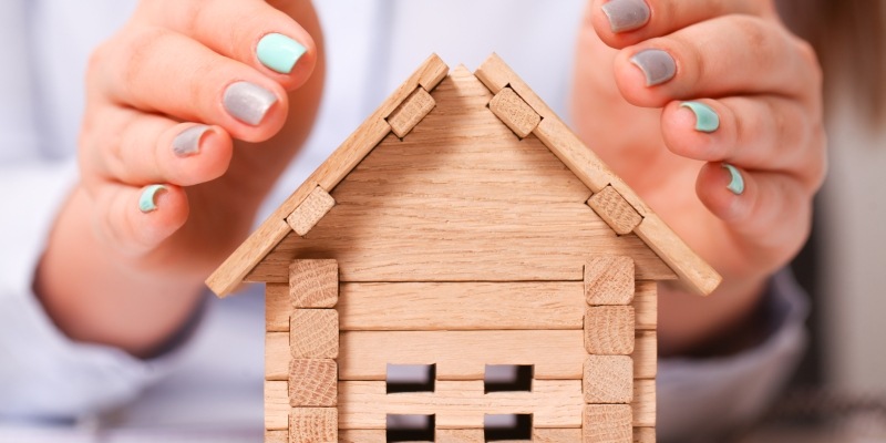 Frau hält schützend ihre Hände über ein kleines Holzhaus