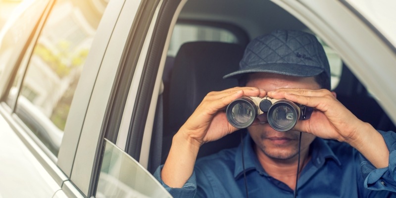 Mann sitzt mit Fernglas in einem Auto und beobachtet