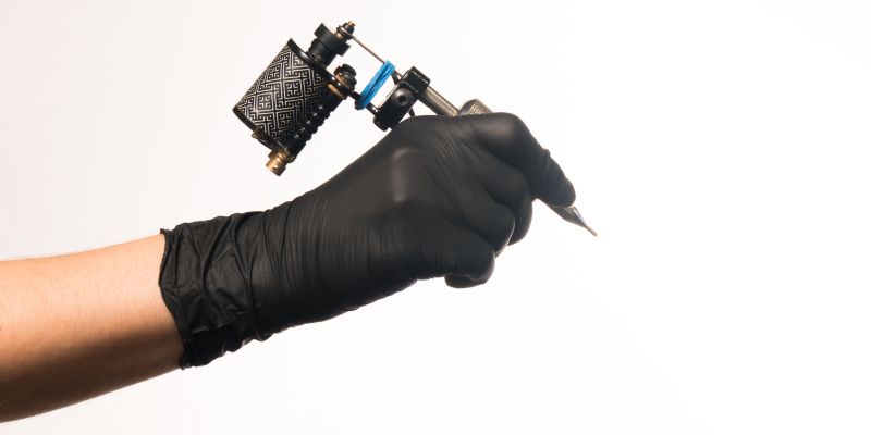Tätowiermaschine in Hand mit schwarzen Handschuhen Tätowiermaschine in Hand mit schwarzen Handschuhen